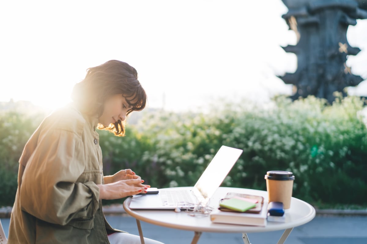 young female digital nomad working on a laptop outside in the sun